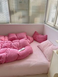 a pink couch with pillows on it in front of a window and windowsills