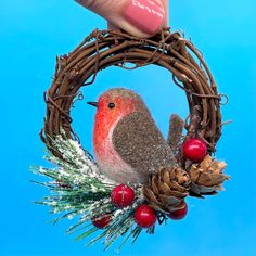 a hand holding a small bird on top of a wreath with berries and pine cones