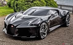 a black sports car parked on top of a gravel road next to a body of water