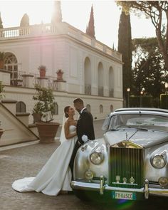 a bride and groom standing in front of an old car with the sun shining on them