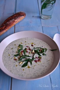 a white bowl filled with soup next to a baguette and bread on a blue table