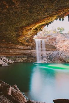 there is a small waterfall in the middle of this cave with green water and rocks