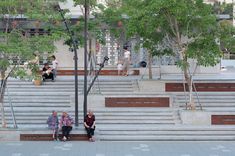 two women are sitting on the steps in front of some trees and stairs with benches