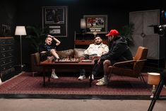 three people sitting around a coffee table playing chess in a room with black walls and red carpet