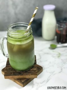 a green drink in a mason jar with a striped straw sitting on a wooden coaster