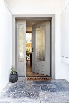 a welcome mat sits on the front door of a white house with an entry way and potted succulents