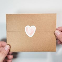 two hands holding up a brown envelope with a heart sticker on the front and back