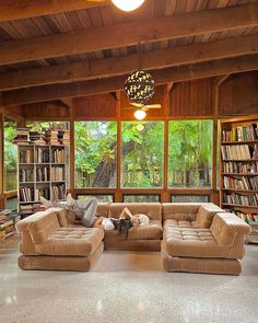 a living room filled with furniture and lots of books on the shelves in front of large windows