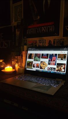 an open laptop computer sitting on top of a wooden desk next to candles and books