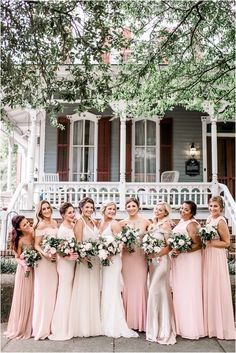 a group of women standing next to each other in front of a white house holding bouquets