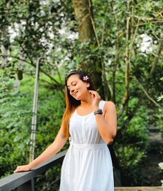 a woman in a white dress is standing on a bridge and talking on her cell phone