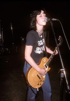 a woman singing into a microphone while holding a guitar