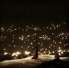 two people are sitting in the snow at night with lights on their head and hands behind them