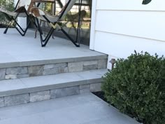 an outdoor patio with steps leading up to the front door and side porch area that has chairs on it