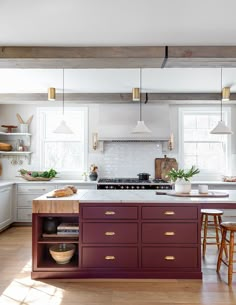 a kitchen with an island, stove and stools next to it in front of two windows