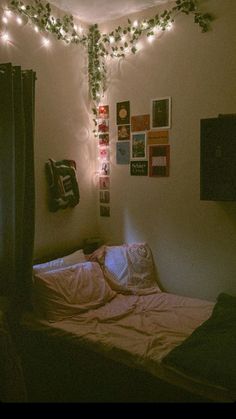 an unmade bed with lights hanging from the ceiling and pictures on the wall above it