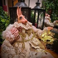 a rabbit doll sitting on top of a table next to some plants and lanterns in the background