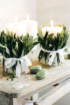 two white candles sitting on top of a wooden table next to flowers and leaves in vases