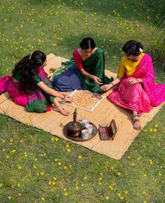 three women are sitting on a blanket in the grass and playing with a board game