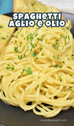 spaghetti with garlic and parsley on a black plate next to toasted baguetta bread