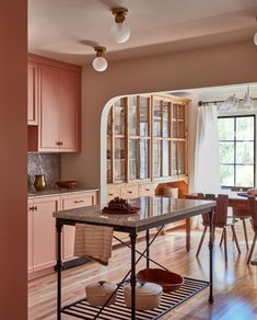 an open kitchen with wooden floors and pink cabinets, along with a dining table in the center