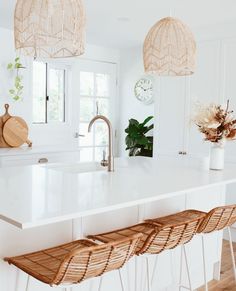 a white kitchen with wicker bar stools and hanging lights above the island counter