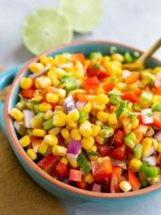 a bowl filled with corn and vegetables on top of a table next to lime wedges