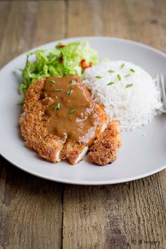 a white plate topped with meat covered in gravy and rice