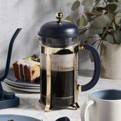 a table topped with plates and cups filled with cake next to a coffee pot covered in frosting