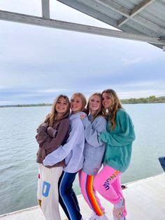 three girls are posing for the camera while standing on a dock by the water with their arms around each other