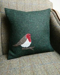 a green pillow with a red and white bird on it sitting on a gray couch