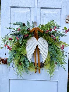 a wreath with angel wings and evergreens is hanging on the front door of a house