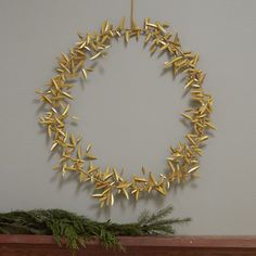 a wreath made out of gold leaves hangs on a wall next to a pine branch