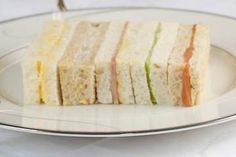 a white plate topped with cut up sandwiches on top of a table next to a knife and fork