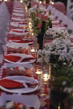 a long table is set with red and white plates, silverware, and flowers