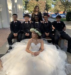 a group of people sitting on top of a wooden bench wearing formal wear and flowers in their hair