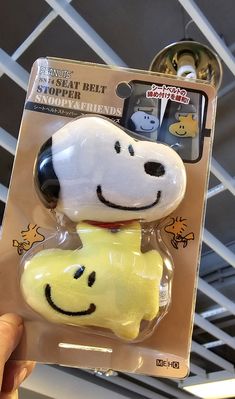 a person holding up a snoopy face and dog head toy in a package for sale