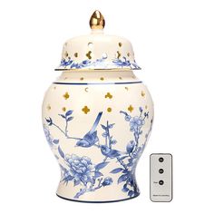 a blue and white vase with a bird on the lid next to a remote control