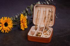 an open suitcase with jewelry in it next to a sunflower on a black surface