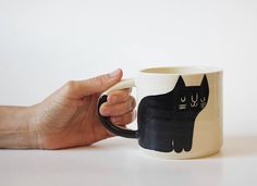 a hand holding a coffee mug with a black cat on it