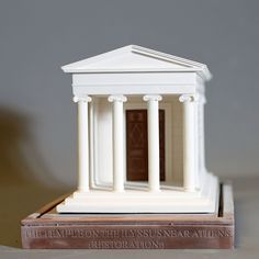 a model of a small white building with columns and pillars on the front, sitting on a wooden base