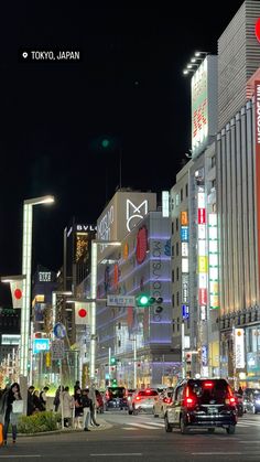 cars are driving down the street at night in tokyo, japan with people walking on the sidewalk