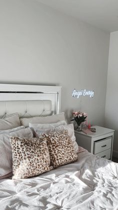 a white bed topped with two pillows next to a night stand and dresser under an angel energy sign