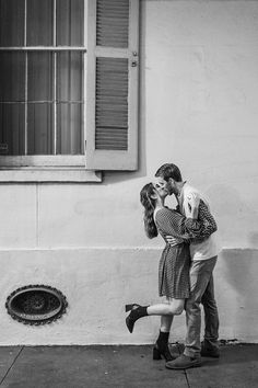 a man and woman kissing in front of a building with a window on the side