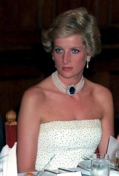 a woman in a white dress wearing a blue and white necklace with pearls on it