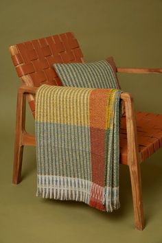 a wooden chair with a plaid blanket draped over the back and arm rests on an olive green background