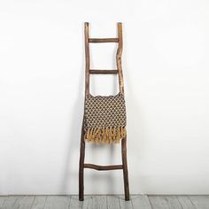 an old wooden ladder leaning against a white wall with a woven bag on it's back