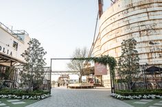 the entrance to an industrial building with plants growing out of it's gates and in between two large silos