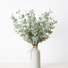 a white vase filled with green leaves on top of a table