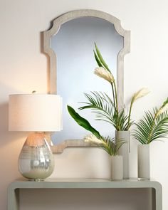 a table with a mirror, lamp and vase on it in front of a white wall